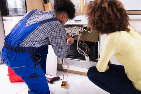 dishwasher repair technician working on a unit as the customer looks on