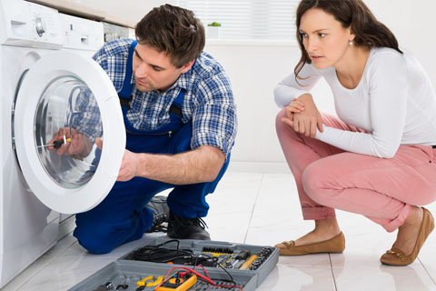 repair technician working on a washing machine while client looks on